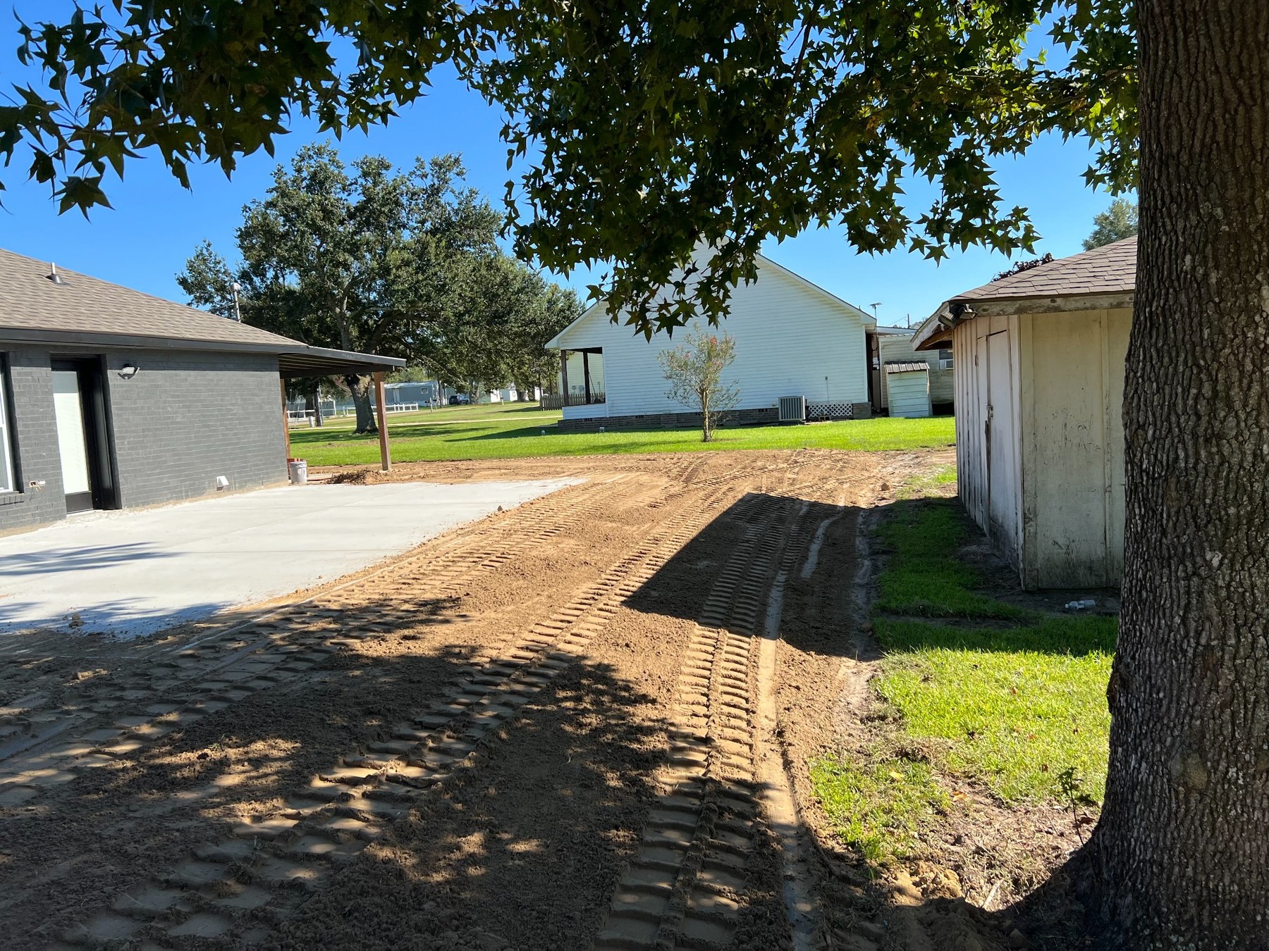 Side yard graded beside a driveway and outbuilding